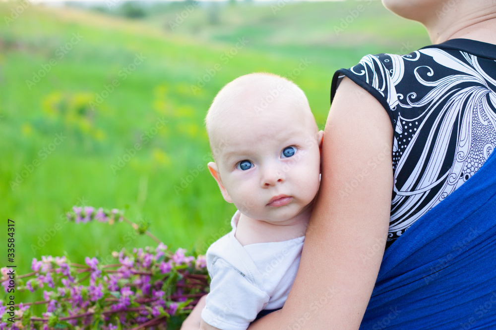 Wall mural baby boy on hands of mother on green meadow