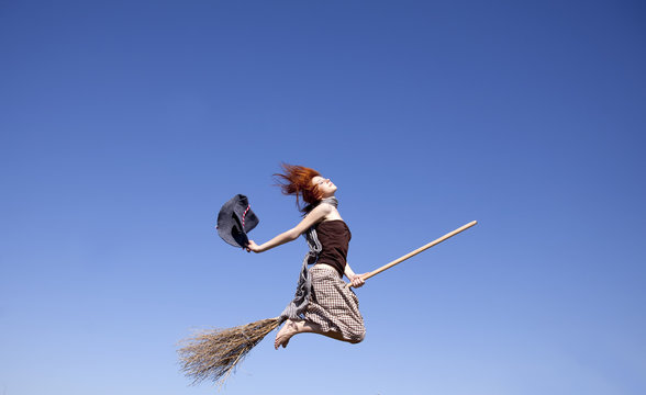Young red-haired witch on broom flying away