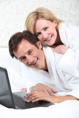 Happy couple on laptop in dressing gown.