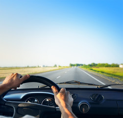 Driver's hands on a steering wheel of a retro car during riding on an empty asphalt road