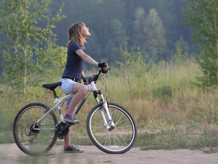 Fototapeta premium Young woman standing with a bicycle on a rural countryside road and looking back
