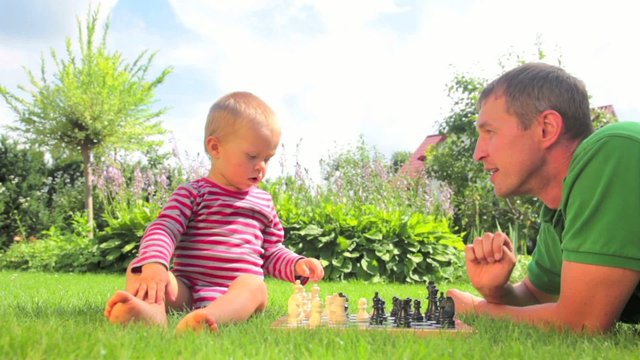 Father and baby playing chess on the grass