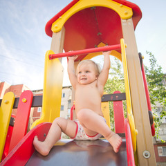 Young adorable baby sliding down baby slide on playground. Prepa