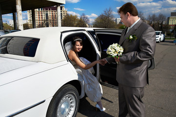 Happy bride and groom out of wedding limousine