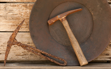 Old mining picks & gold pan against wood background.