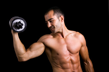 Young muscular man lifting dumbbells against black background