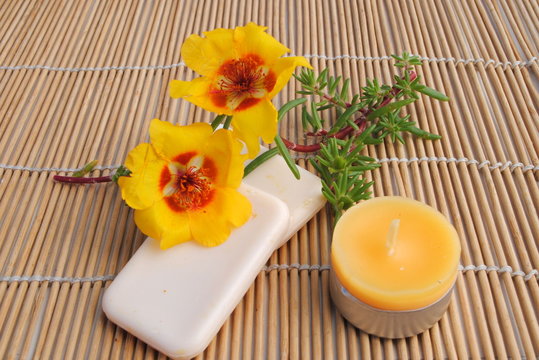 candela e sapone su stuoia di bamboo con fiori gialli