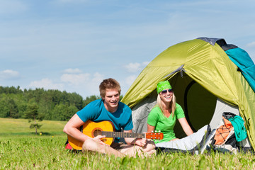 Camping couple playing guitar by tent countryside