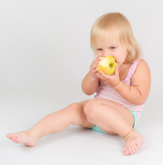 Adorable toddler girl eat green fresh apple sitting on white