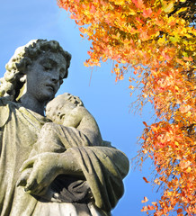 Statue of Virgin Mary holding Baby Jesus under autumn leaves