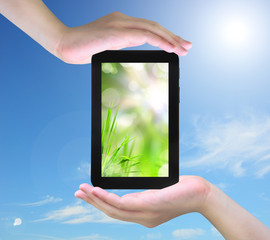 fresh grass and tablet PC in women hand on sky
