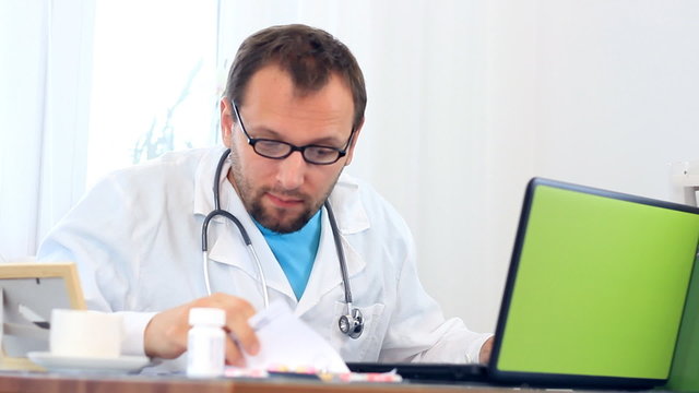 Male doctor working on computer and looking into documents