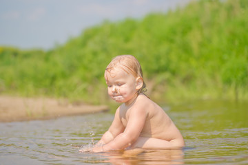 Adorable baby sit in river and play with sand and water