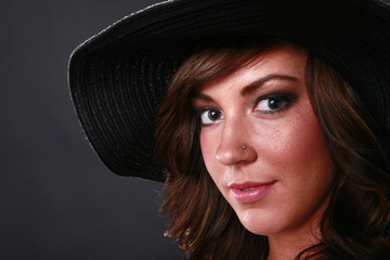 Head shot of a young brunette wearing a hat on black