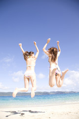 浜辺でジャンプする水着を着た2人の女性の後ろ姿