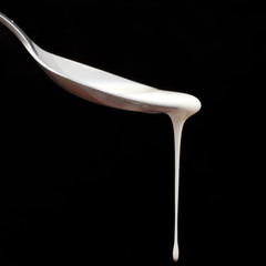 Cream dripping off a spoon, black background.