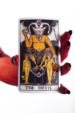 Devil's hand holding a tarot card, white background.