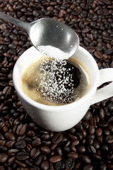 sugar pouring with spoon in a cup of espresso coffee.
