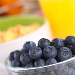 Blueberries in glass bowl with cereal and orange juice