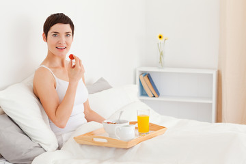 Obraz na płótnie Canvas Smiling brunette eating a strawberry