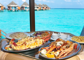 Two plates with lobster on table at window with view on ocean.. - 33913307