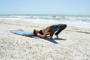 woman doing yoga exercise on beach in bridge pose