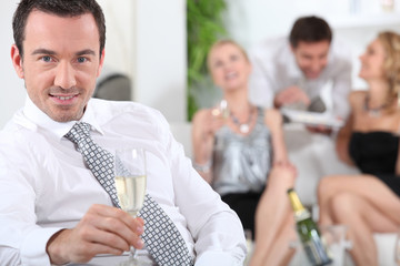 Man sitting holding champagne glass friends in background