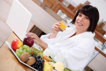 Obraz na płótnie Canvas Woman using a laptop while eating a fruity breakfast