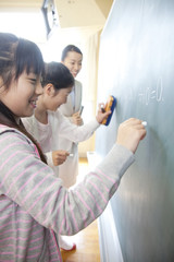 黒板の問題を解く小学生女子と横に立つ女性教師