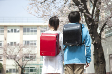 桜の下に立つ小学生男女の後ろ姿