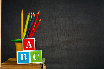 ABC and multicolored pencil on old textbook against blackboard