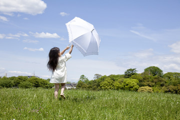 日傘を差して草原を歩く女の子の後ろ姿