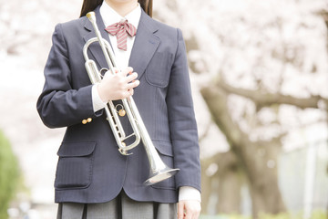 桜の下でトランペットを持っている女子中学生