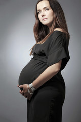 Pregnant woman with long dark hair in black dress.