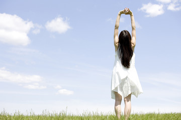 草原で両手を上げる女性の後ろ姿
