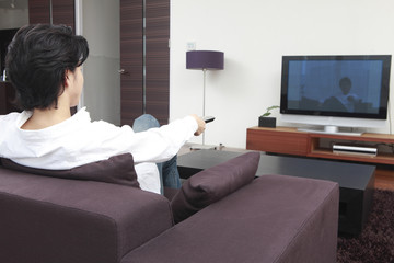 リモコンでテレビをつけようとする男性の後姿