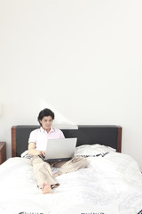ベッドの上でノートパソコンに向かう男性