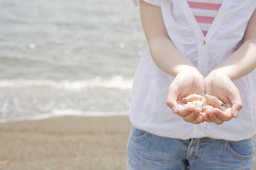 砂浜で貝殻を手に持つ女性