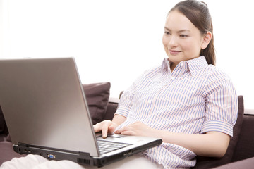 ソファーに座りながらノートパソコンをする女性