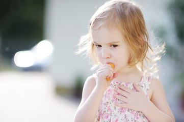 Adorable happy preschooler girl eating carrot outdoors