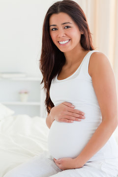Portrait of a good looking pregnant woman touching her belly whi