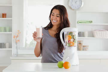 Attractive woman using a blender while holding a drink
