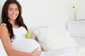 Beautiful pregnant woman holding an apple on her belly while lyi