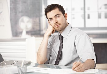 Young man working in office writing notes thinking
