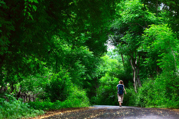Young woman walking on green asphalt road in the forest