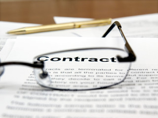 Reading glasses on papers and word "contract"in focus