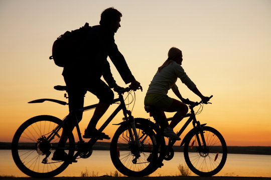 Young couple riding bicycles at sunset.
