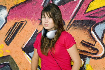 Beautiful brunette girl with headphones and graffiti wall at bac