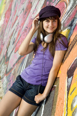 Beautiful brunette girl with headphones and graffiti wall at bac