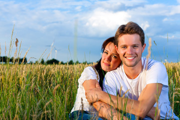 Happy couple sitting on a meadow or grainfield